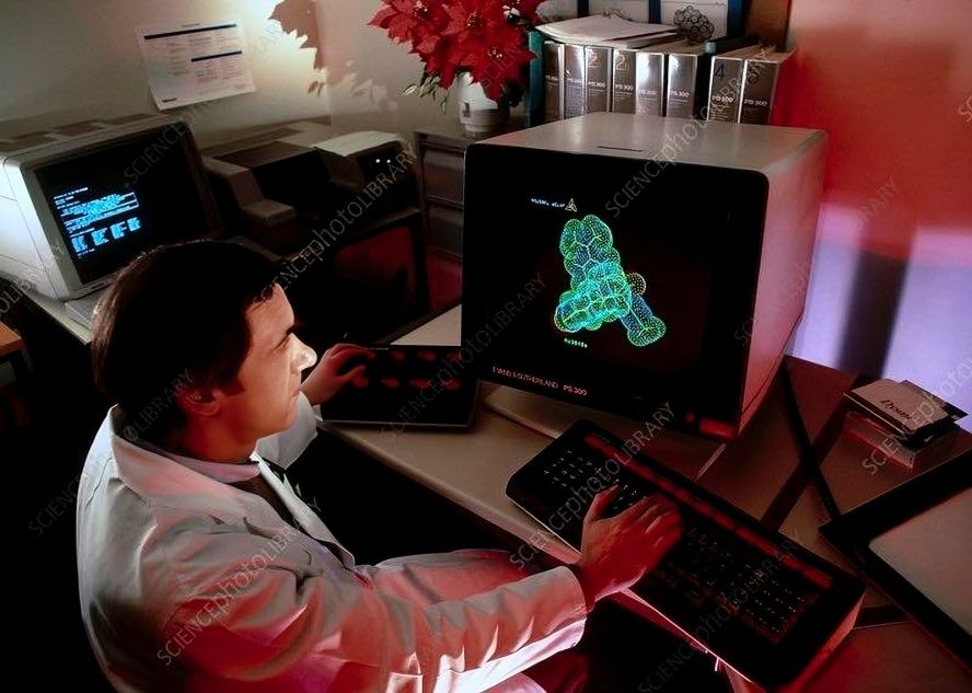 A man is sitting in front of a computer, the screen displays the 3D structure of a molecule.